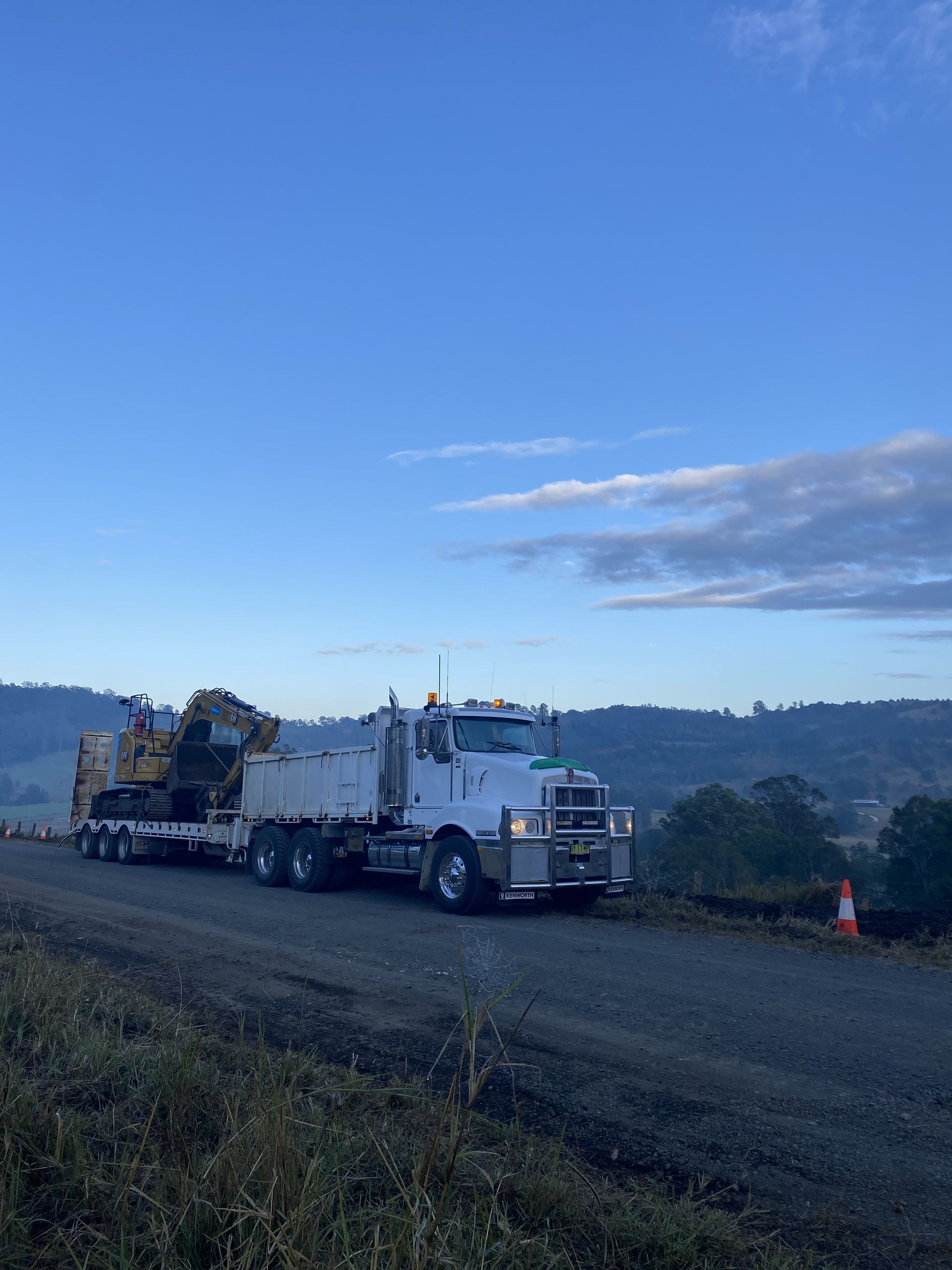A Large Truck Hauling an Excavator on a Low-loader Trailer Travels on a Dirt Road — PVM Contracting in Alstonville, NSW