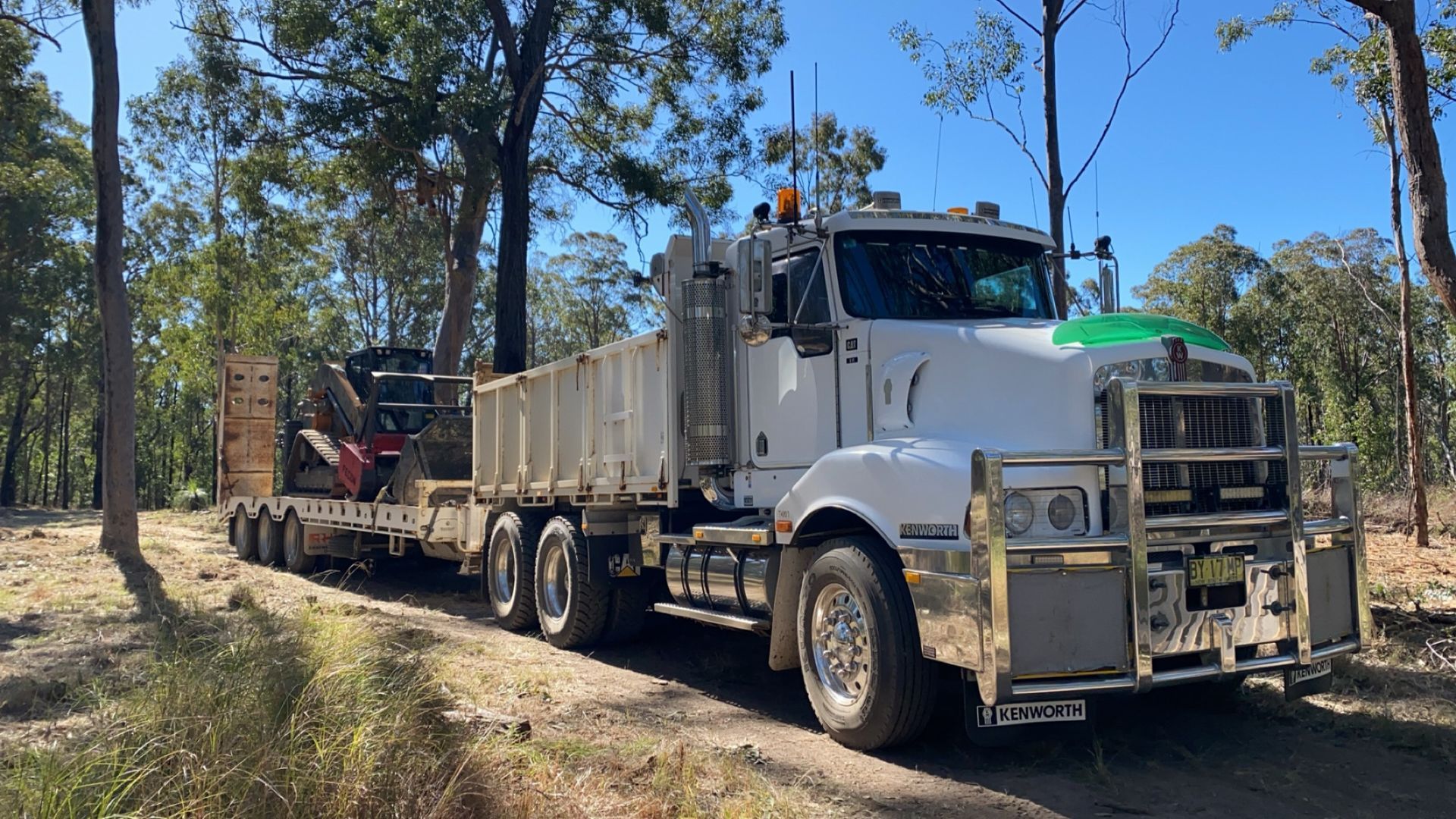 A White Semi-truck Hauling Construction Equipment on a Dirt — PVM Contracting in Yamba, NSW