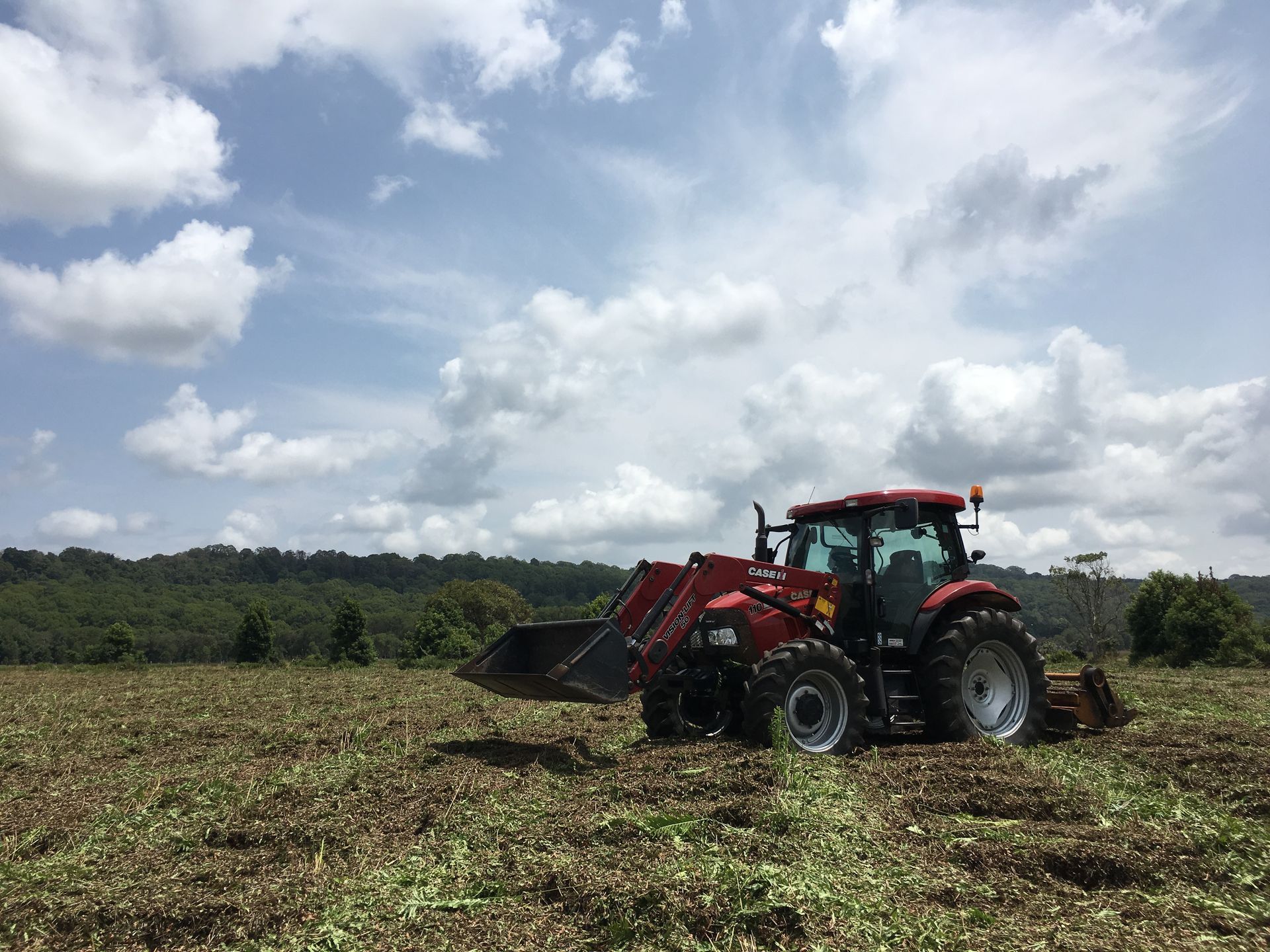 A Red Tractor With a Front Loader Working in a Field — PVM Contracting in Alstonville, NSW