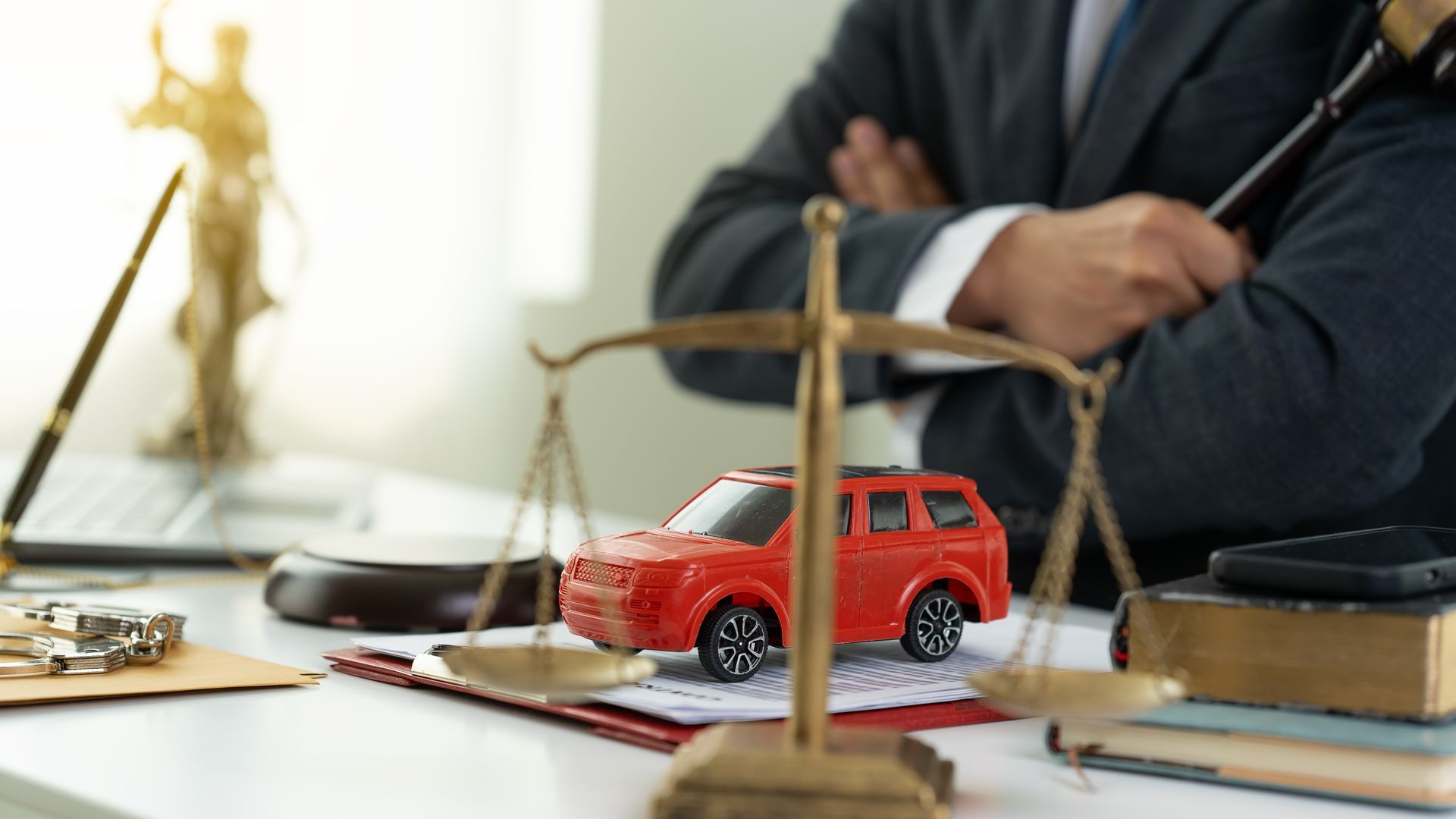 An auto accident attorney is holding a gavel and sitting at a table with a miniature car and balance