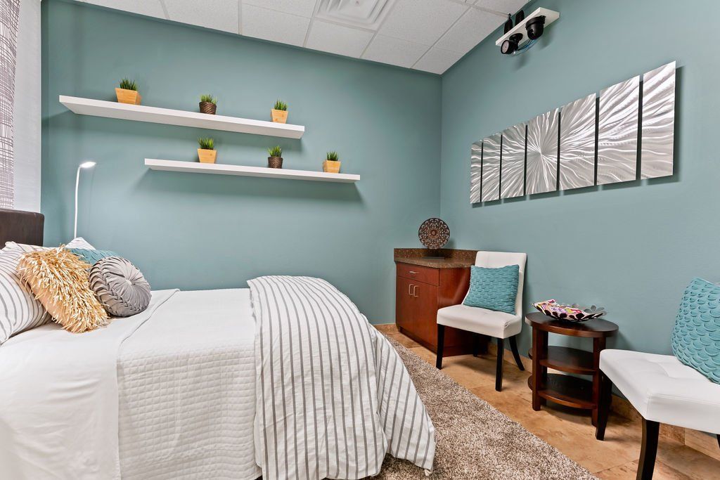 A bedroom with a bed , chair , table and shelves. | United Critical Care