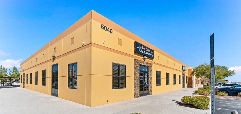 A large yellow building with a lot of windows and a parking lot in front of it. | United Critical Care