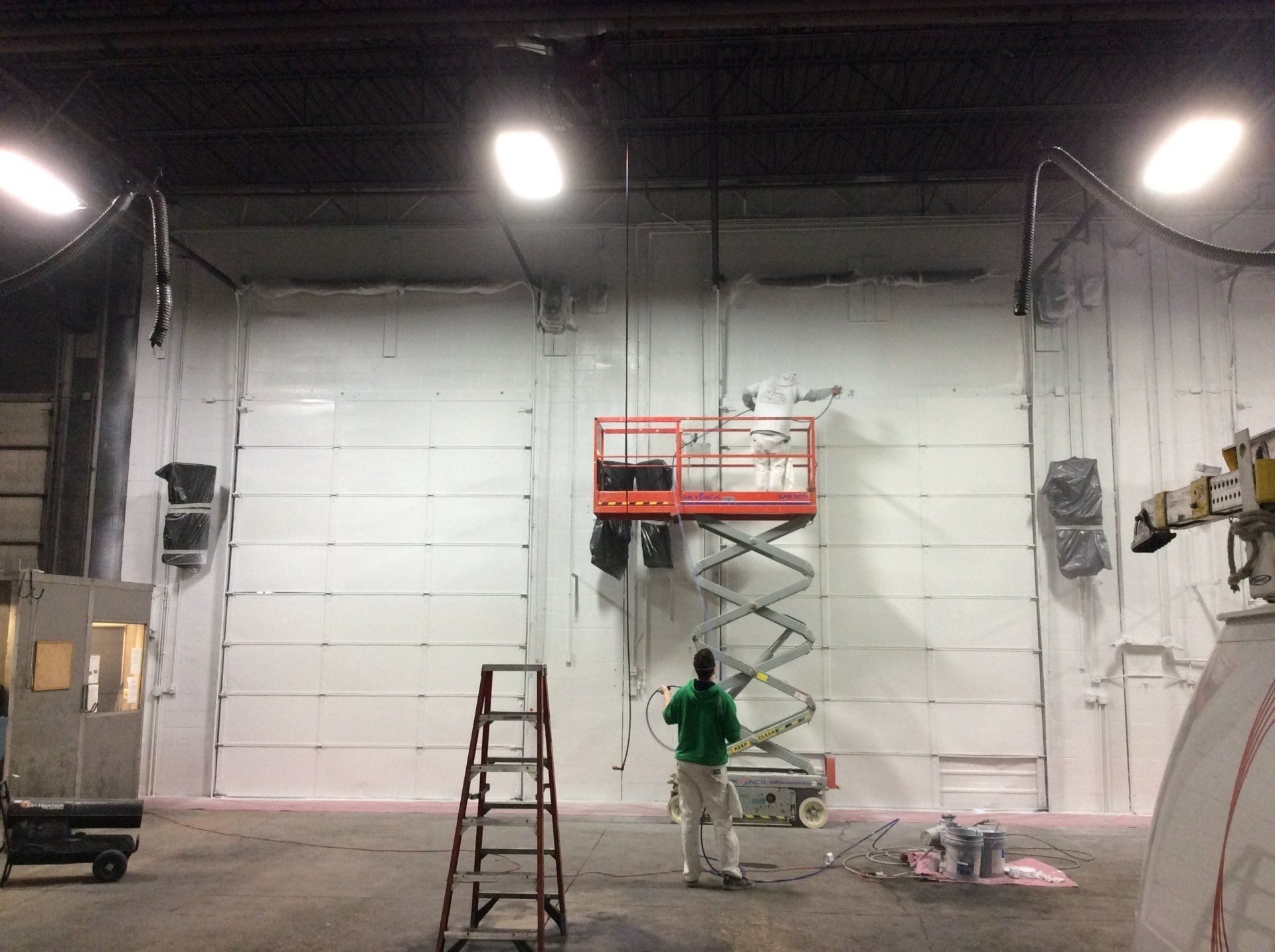a man is standing on a ladder in a warehouse painting a wall .
