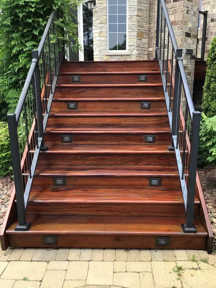 Wooden outdoor staircase with black railings leading to a stone entryway