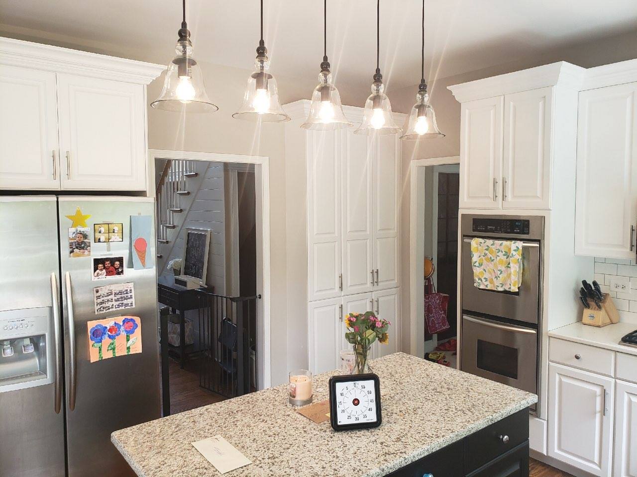 a kitchen with white cabinets , granite counter tops , stainless steel appliances and a clock on the island .