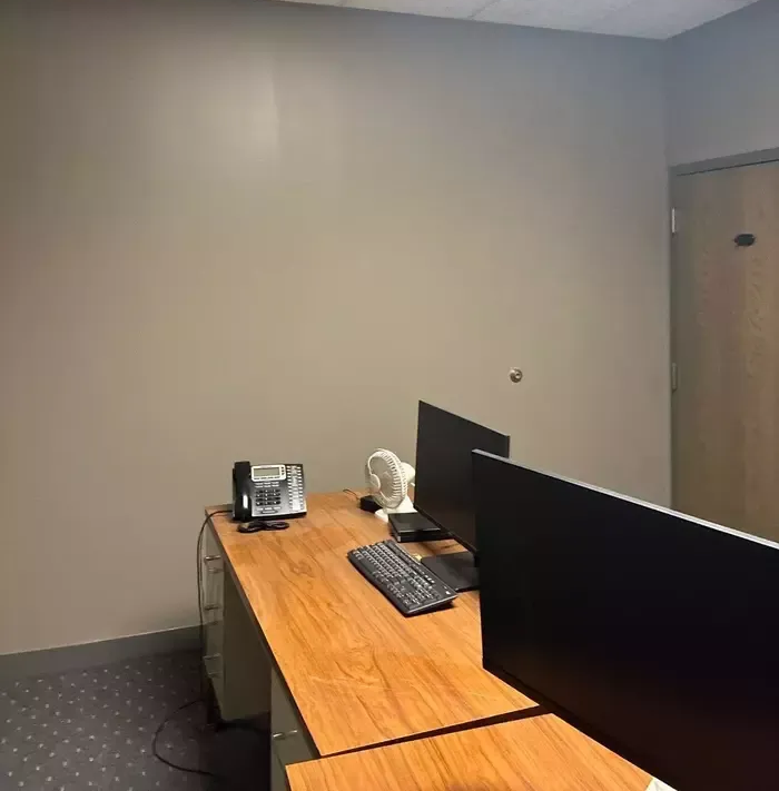 Empty office cubicle with wooden desk, dual monitors, keyboard, and gray walls