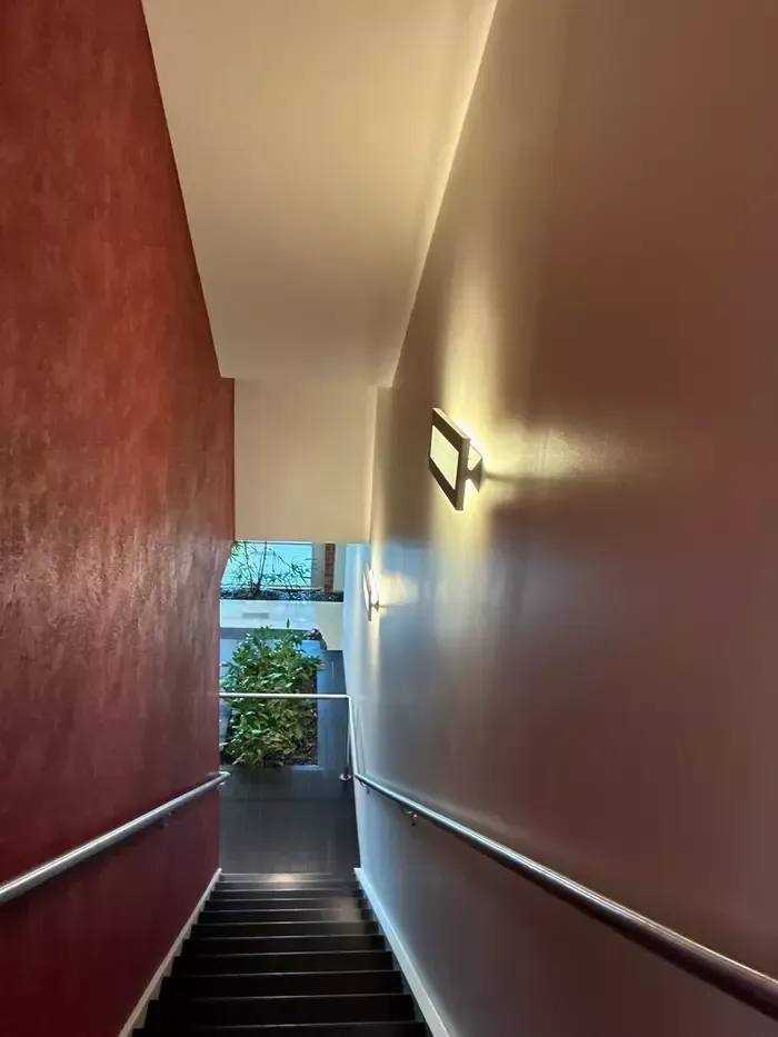 Narrow stairwell with red and white walls, handrails, and daylight visible at the bottom.