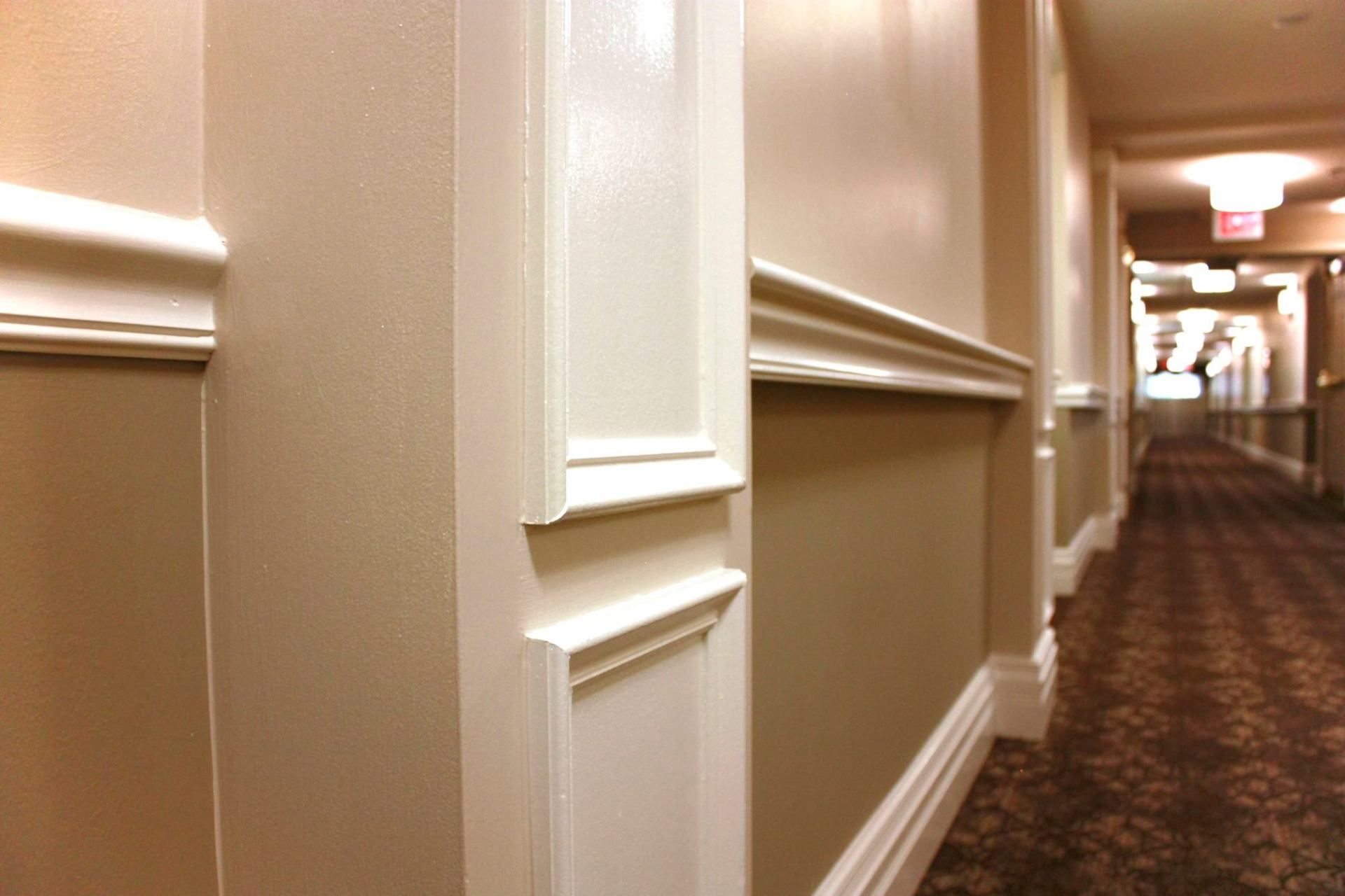 Long hotel hallway with beige walls, white trim, and patterned carpet