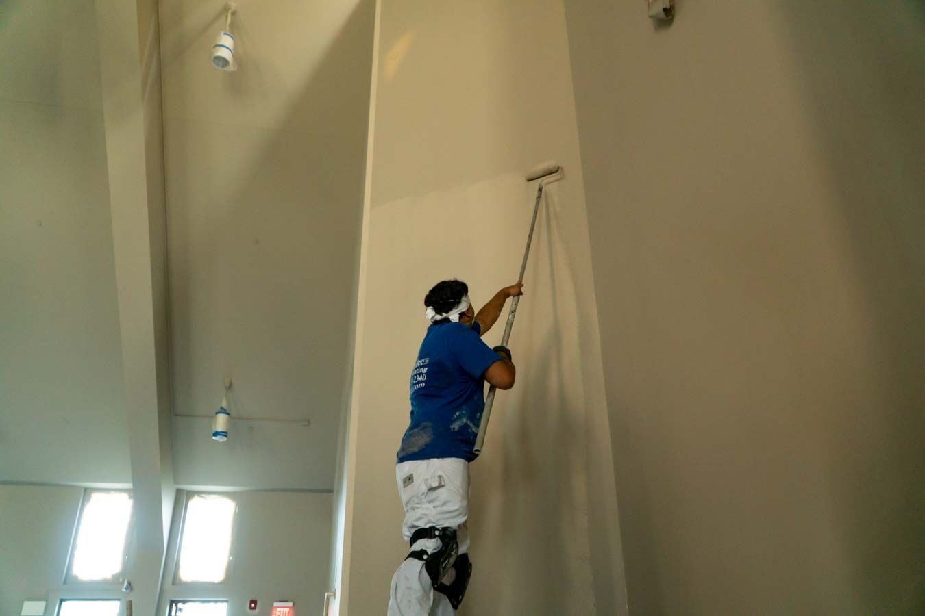 a man in a blue shirt is painting a wall with a roller .