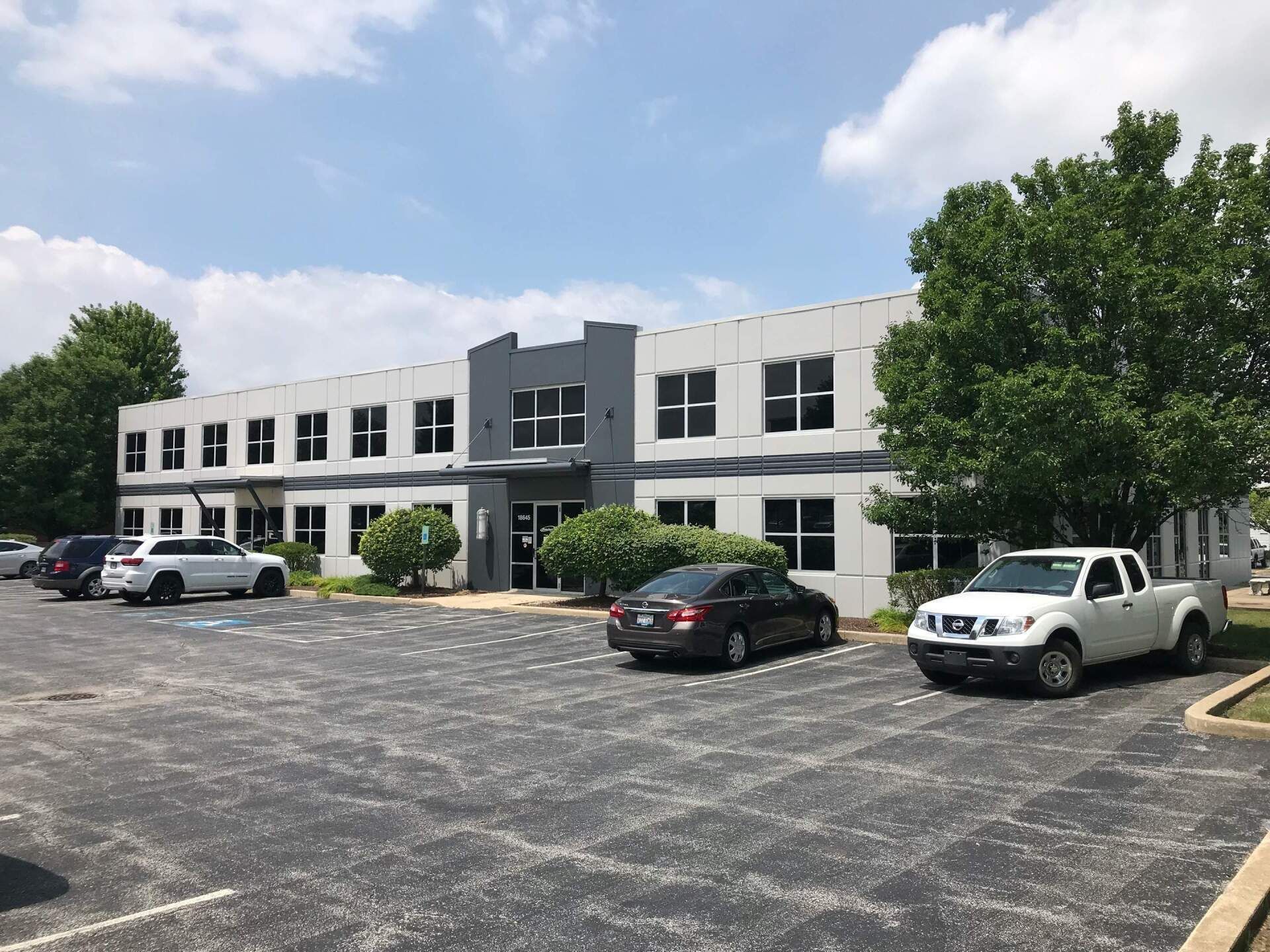 Two-story white office building with parked cars in a sunny lot