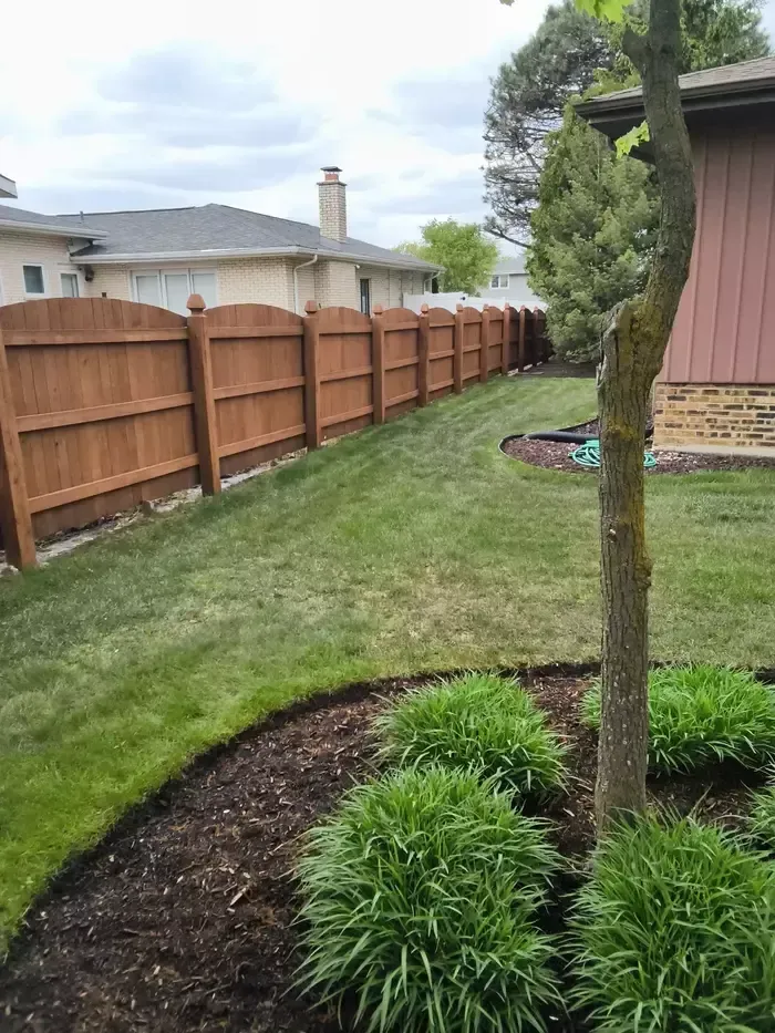 Backyard with wooden fence, green lawn, mulched tree bed, and a small pond in the corner