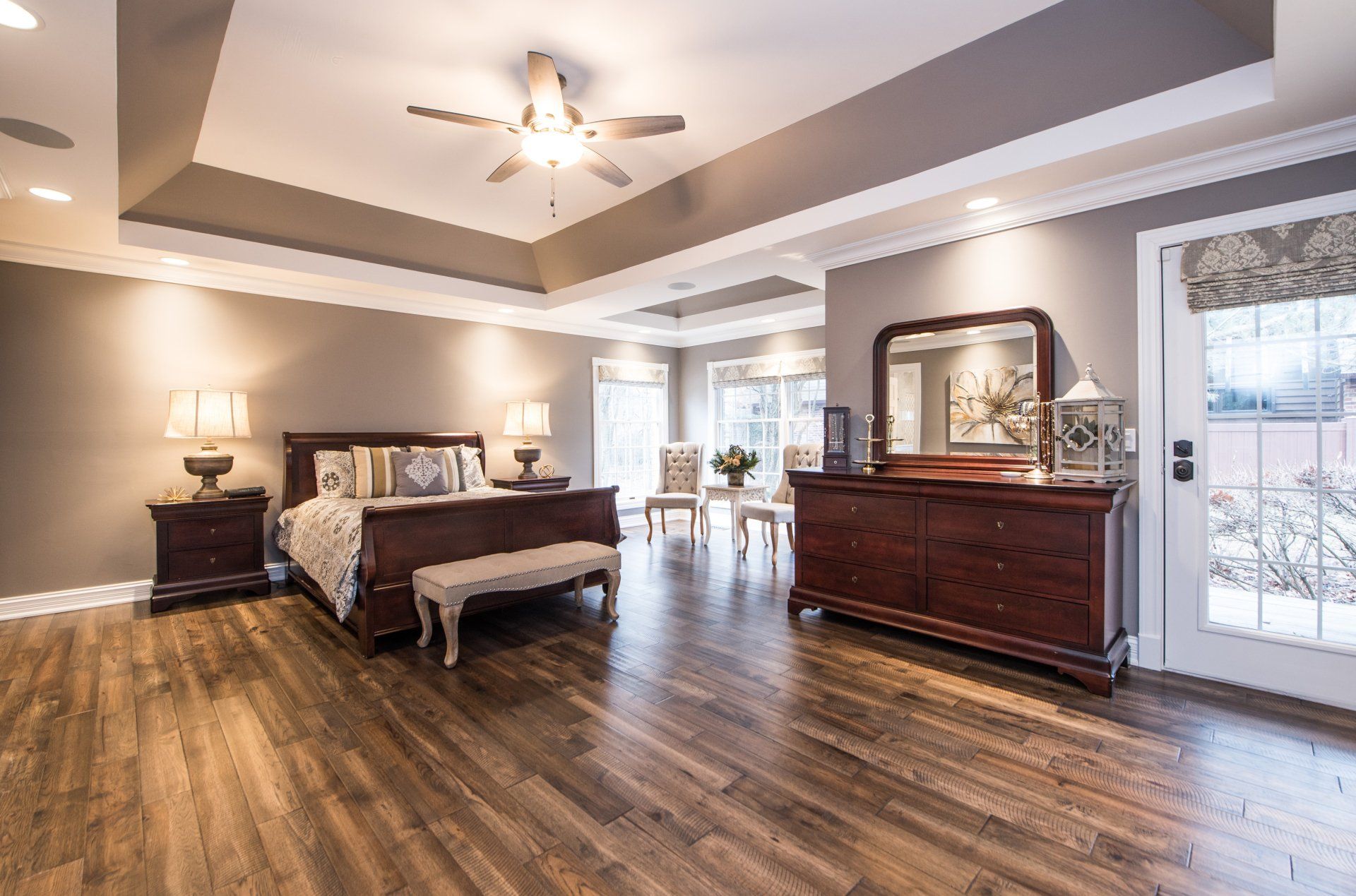 a large bedroom with hardwood floors , a bed , dresser , mirror and ceiling fan .