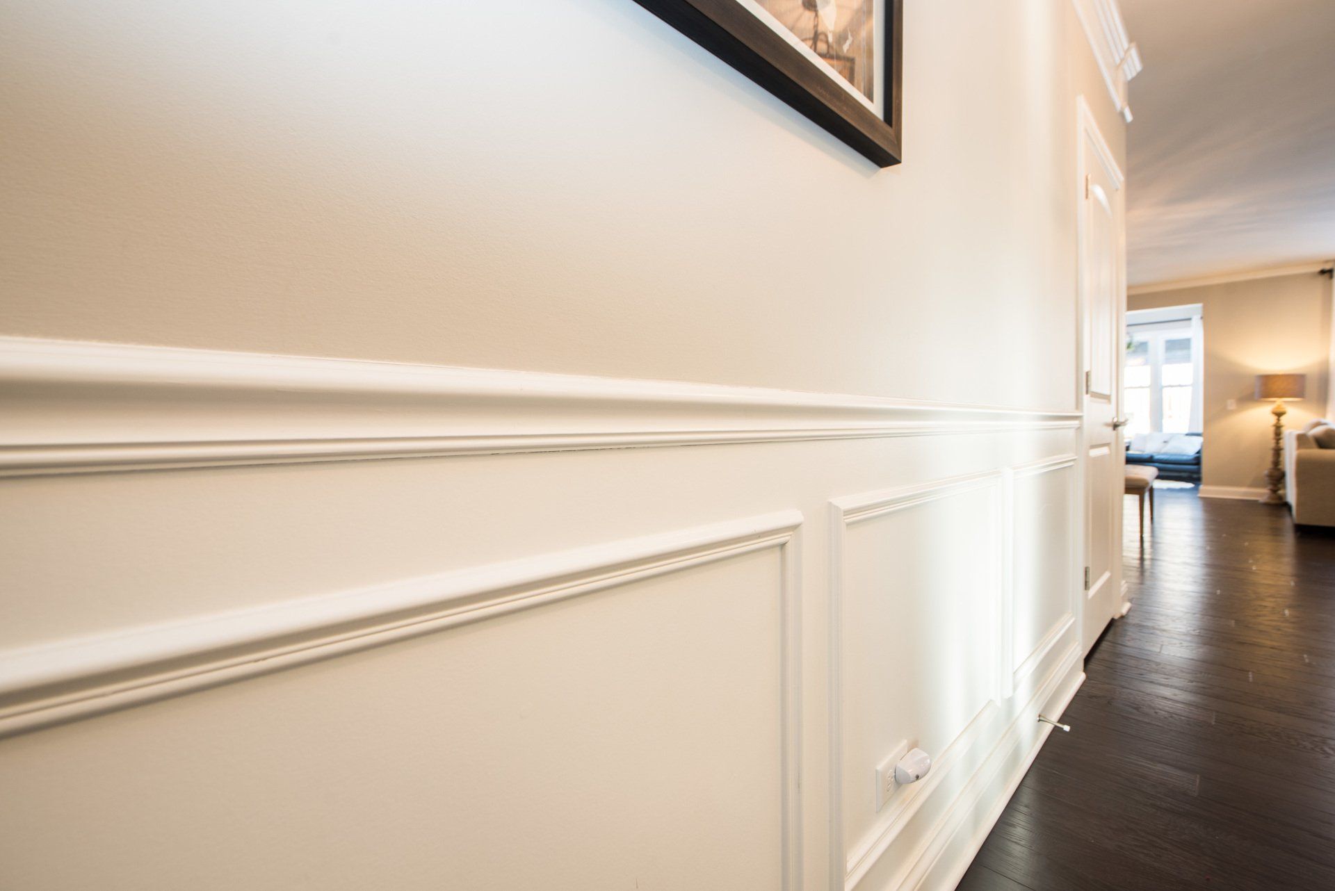 a hallway with white wainscoting and a picture on the wall .