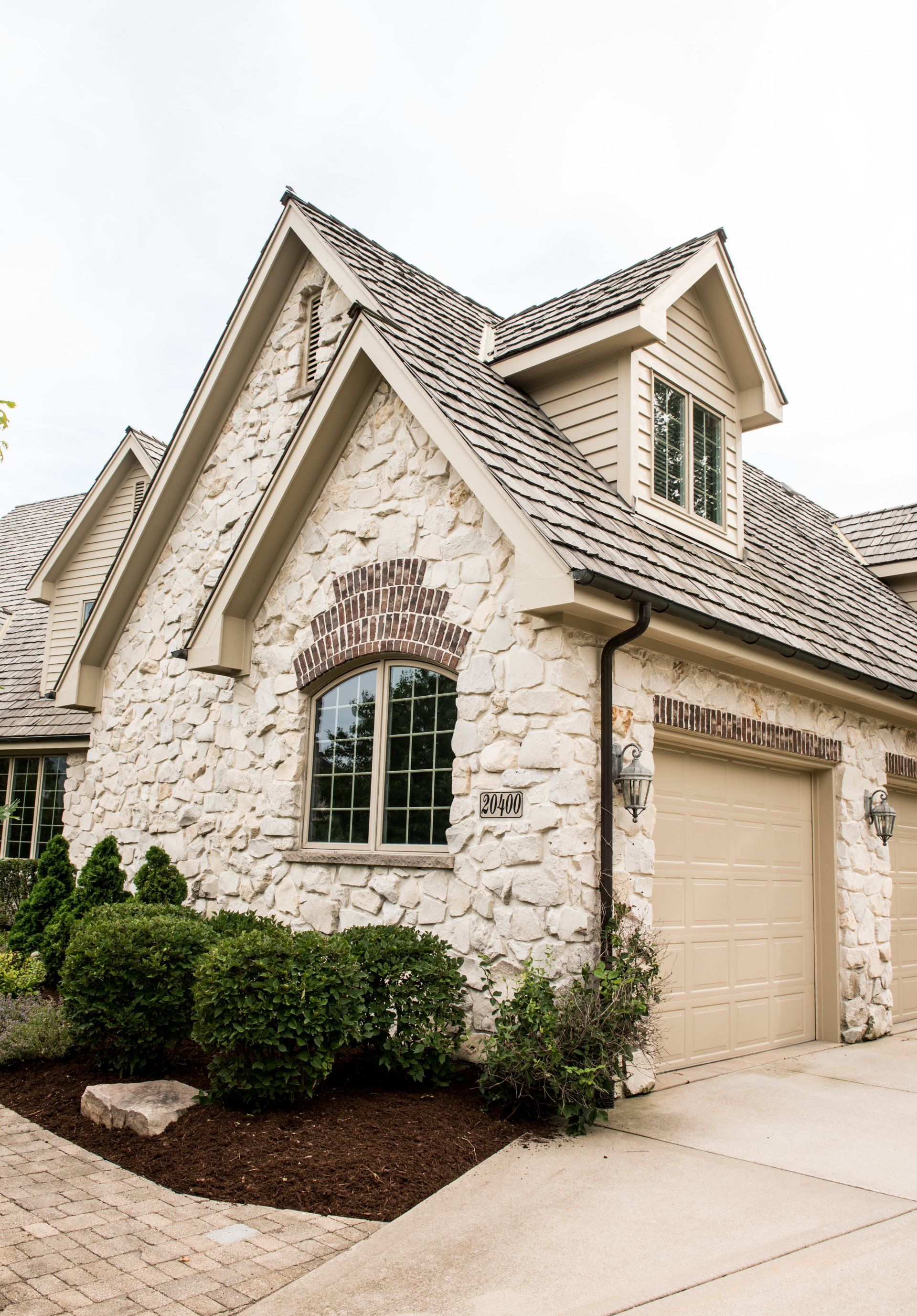 a large stone house with two garage doors and a gray roof .