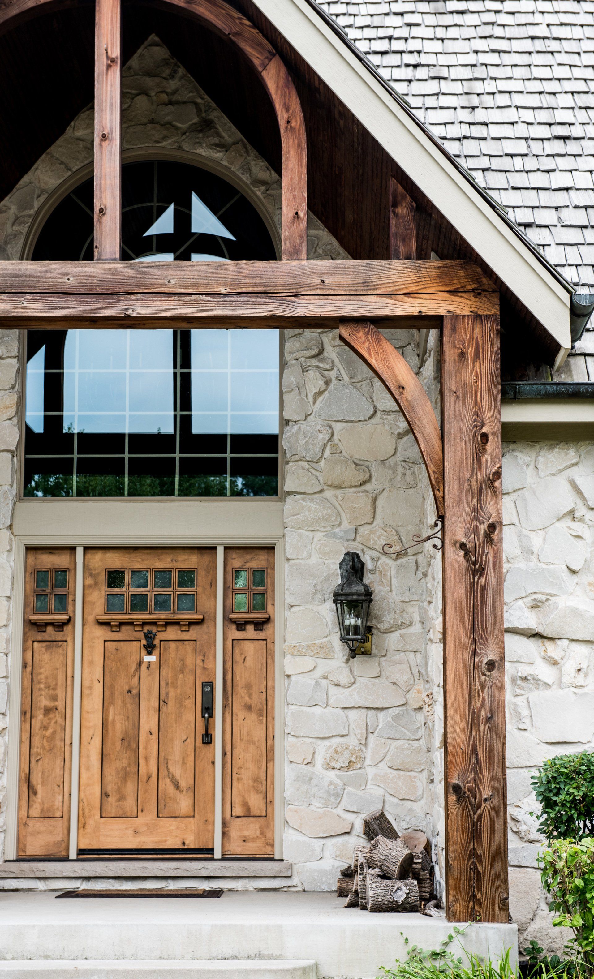 the front door of a stone house with wooden doors and a wooden porch .