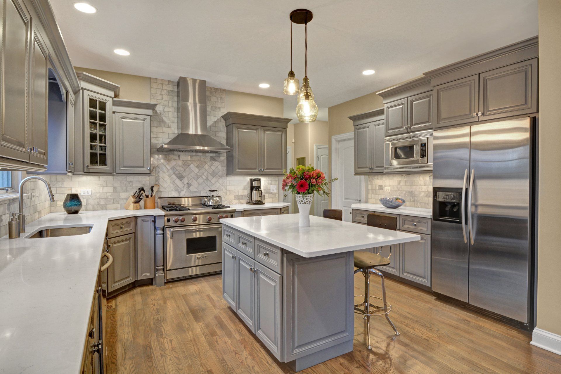 a kitchen with gray cabinets , stainless steel appliances , and a large island .