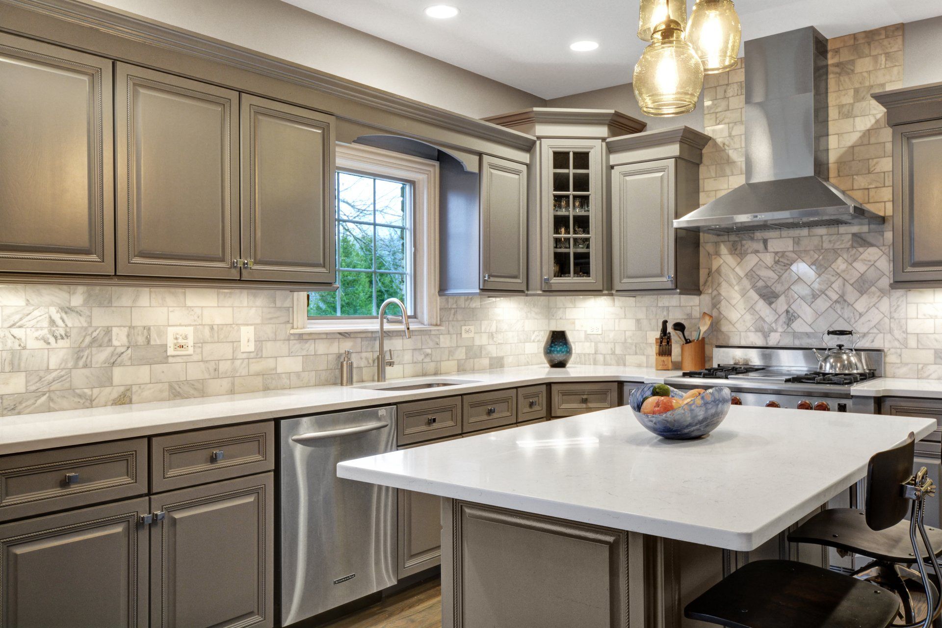 a kitchen with gray cabinets , white counter tops , stainless steel appliances and a large island .