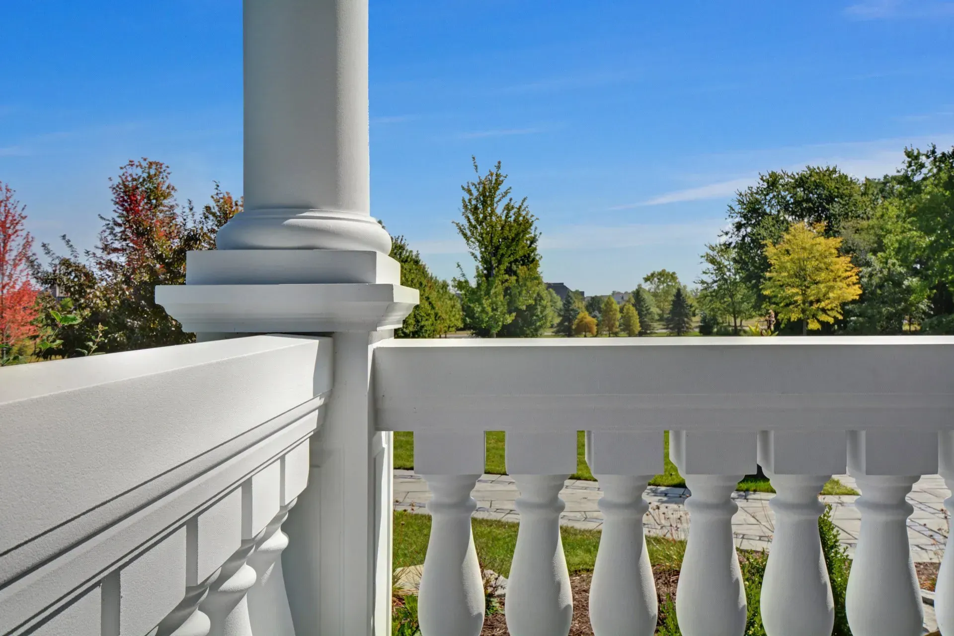 White porch railing and column overlooking colorful autumn trees under a clear blue sky.