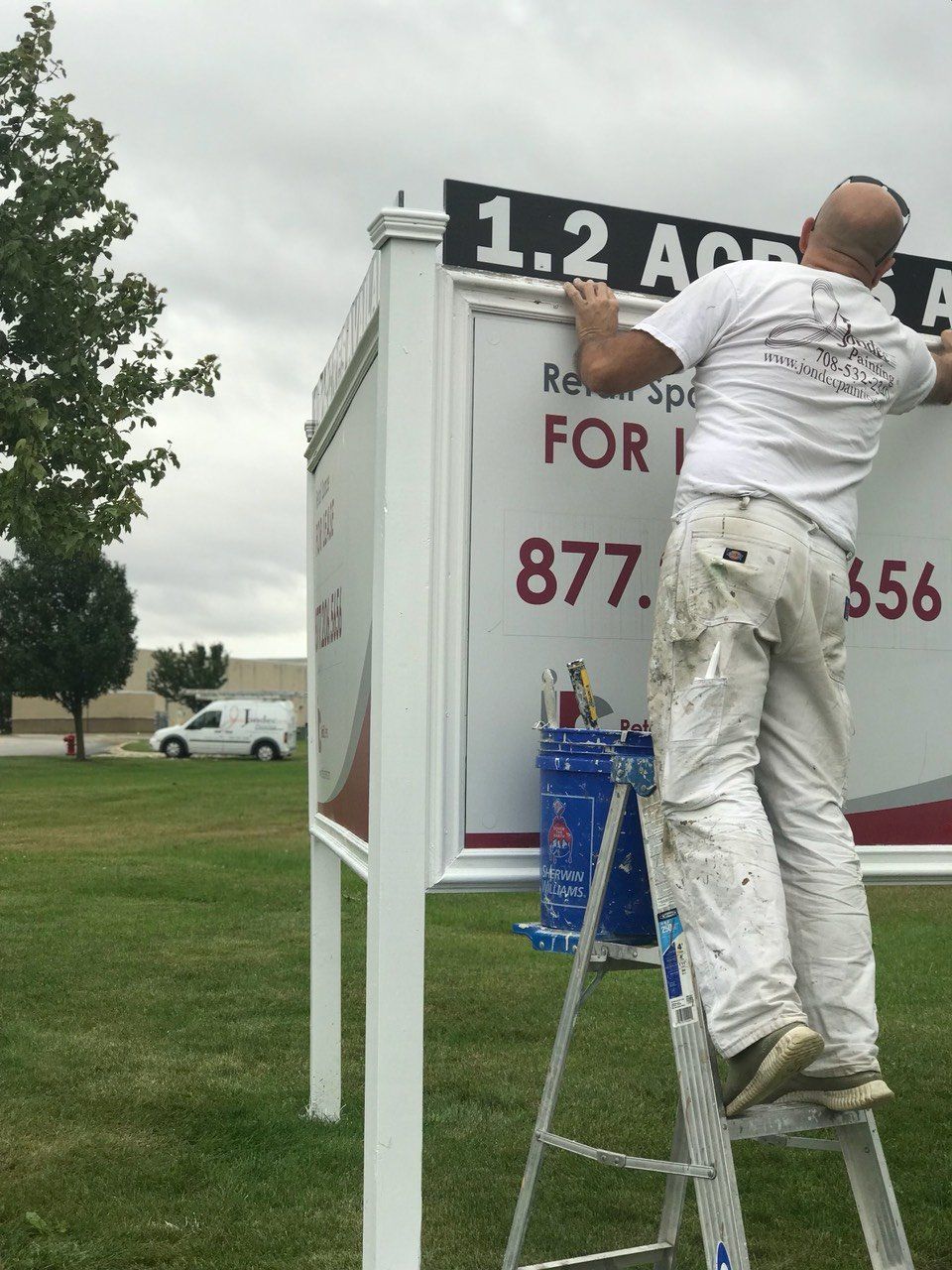 a man on a ladder paints a sign that says 1.2 acre