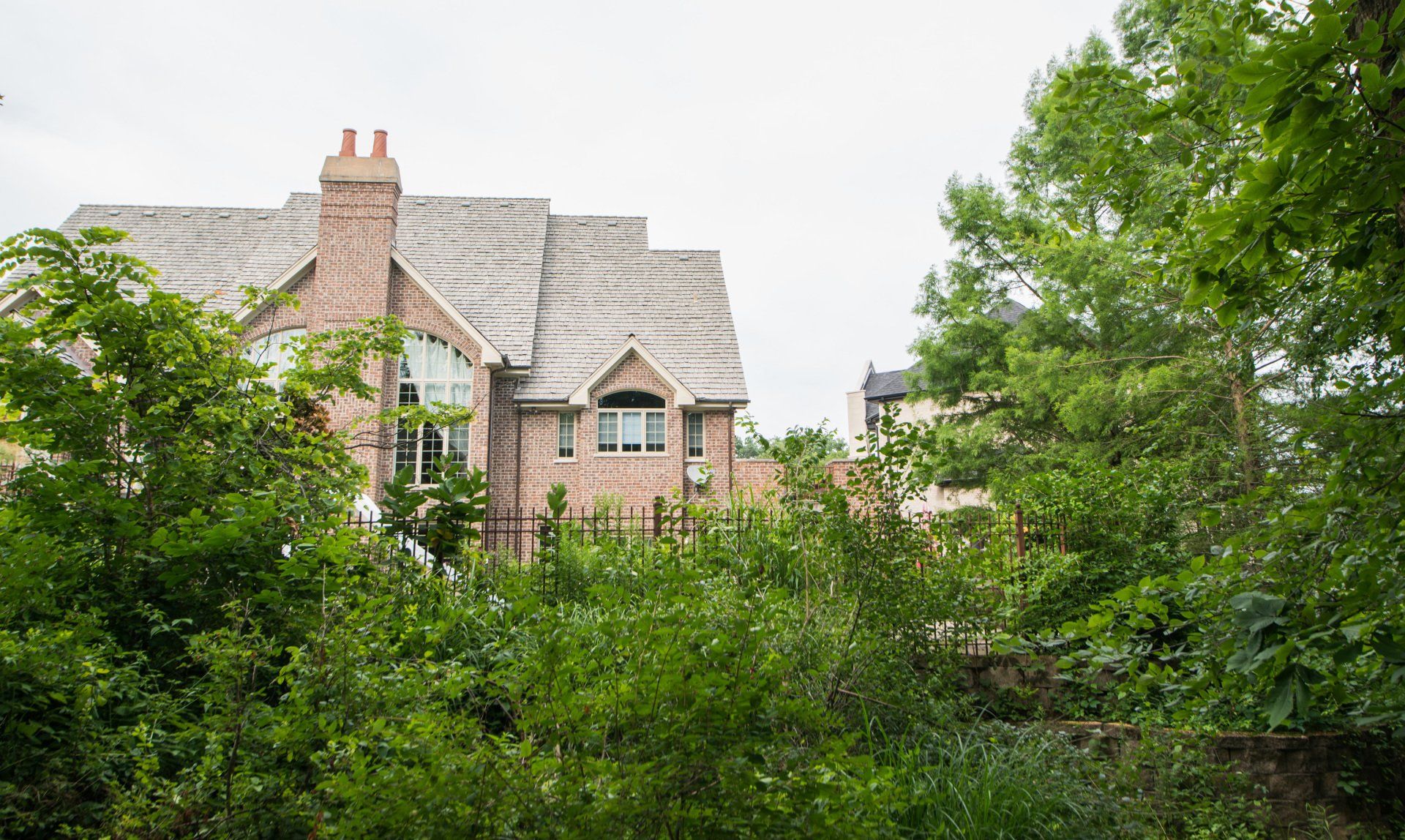 a large brick house is surrounded by trees and bushes .