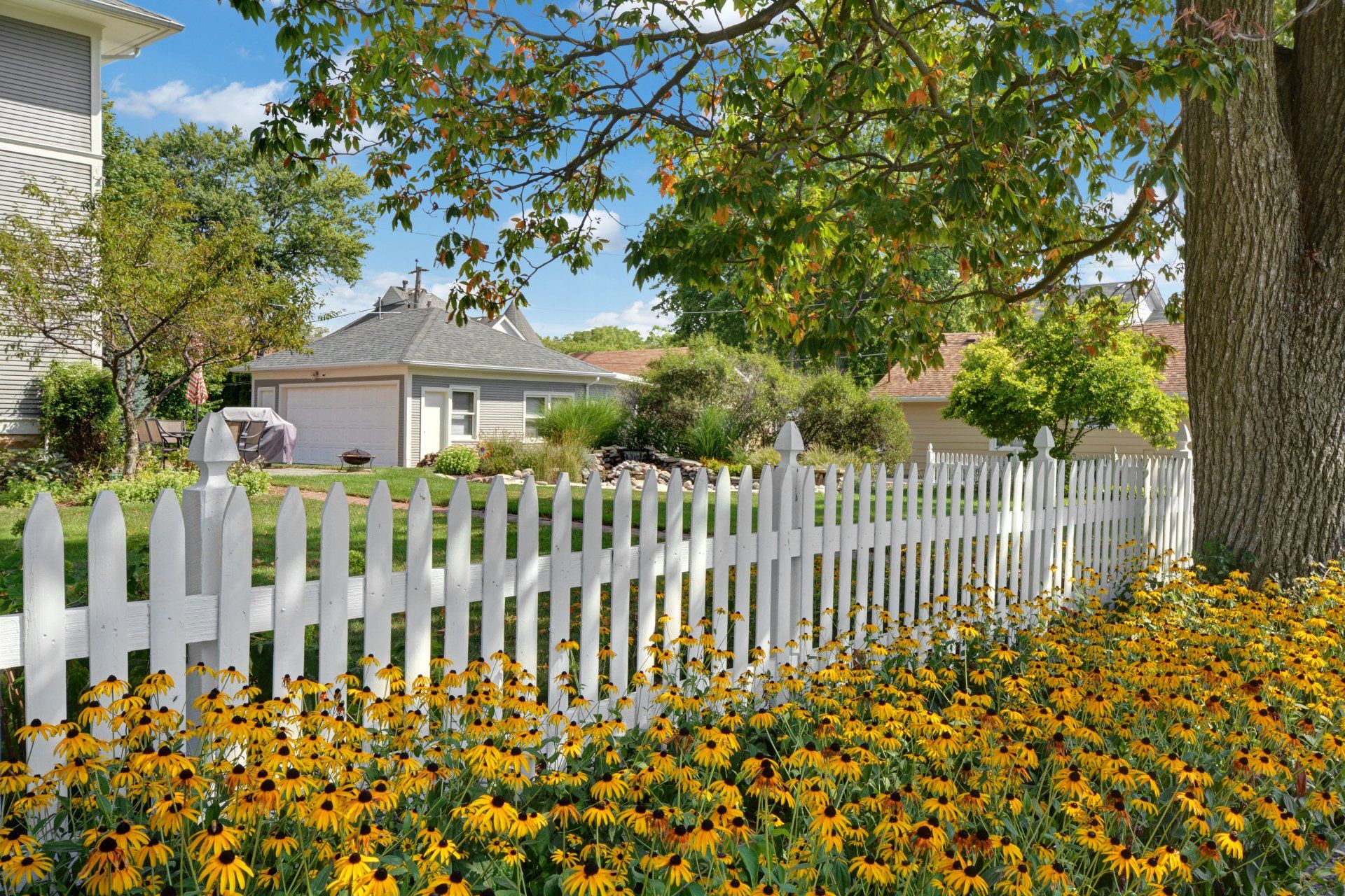 a white picket fence surrounded by yellow flowers in front of a house