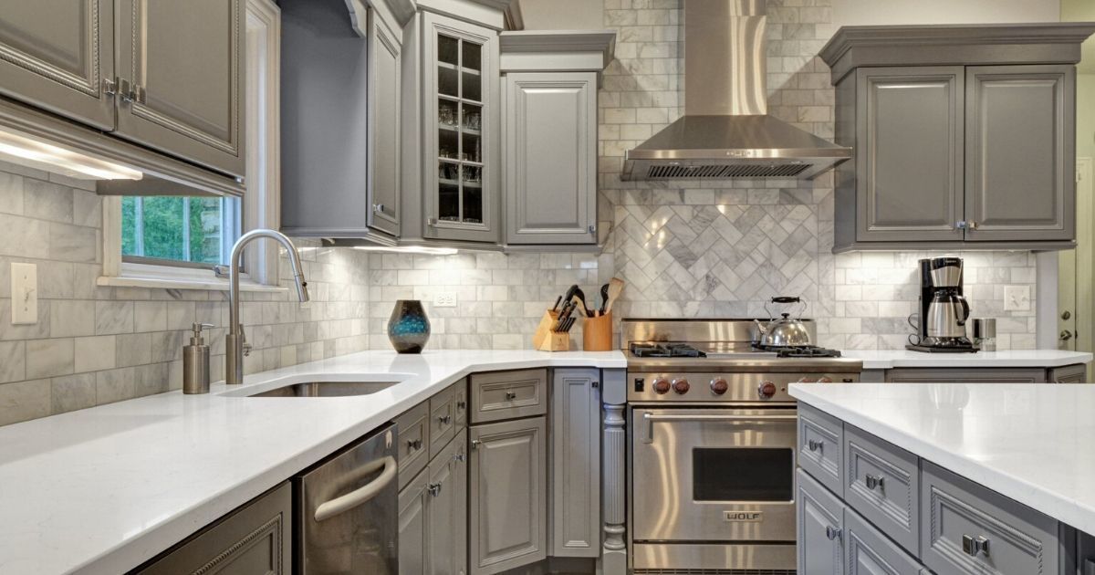 a kitchen with gray cabinets , stainless steel appliances , and white counter tops .
