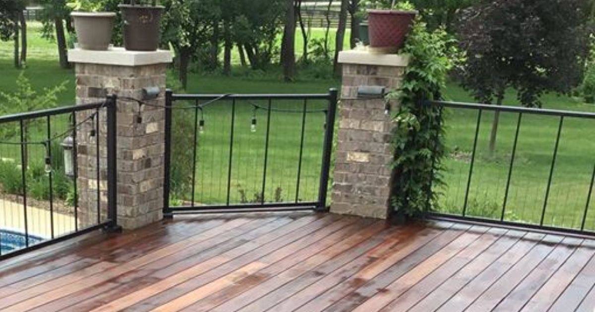 Wet wooden deck with black metal railings and stone pillars overlooking a green yard
