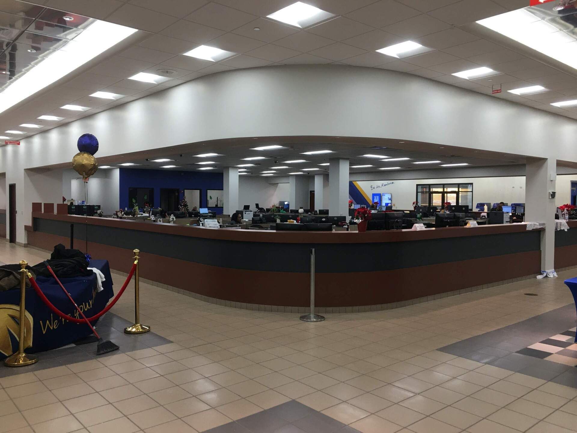 Wide indoor lobby with a curved counter, tiled floor, and ceiling lights; a balloon display at left.