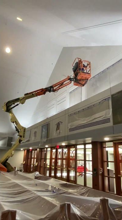 Orange boom lift reaching up inside a building with covered floors and tall windows