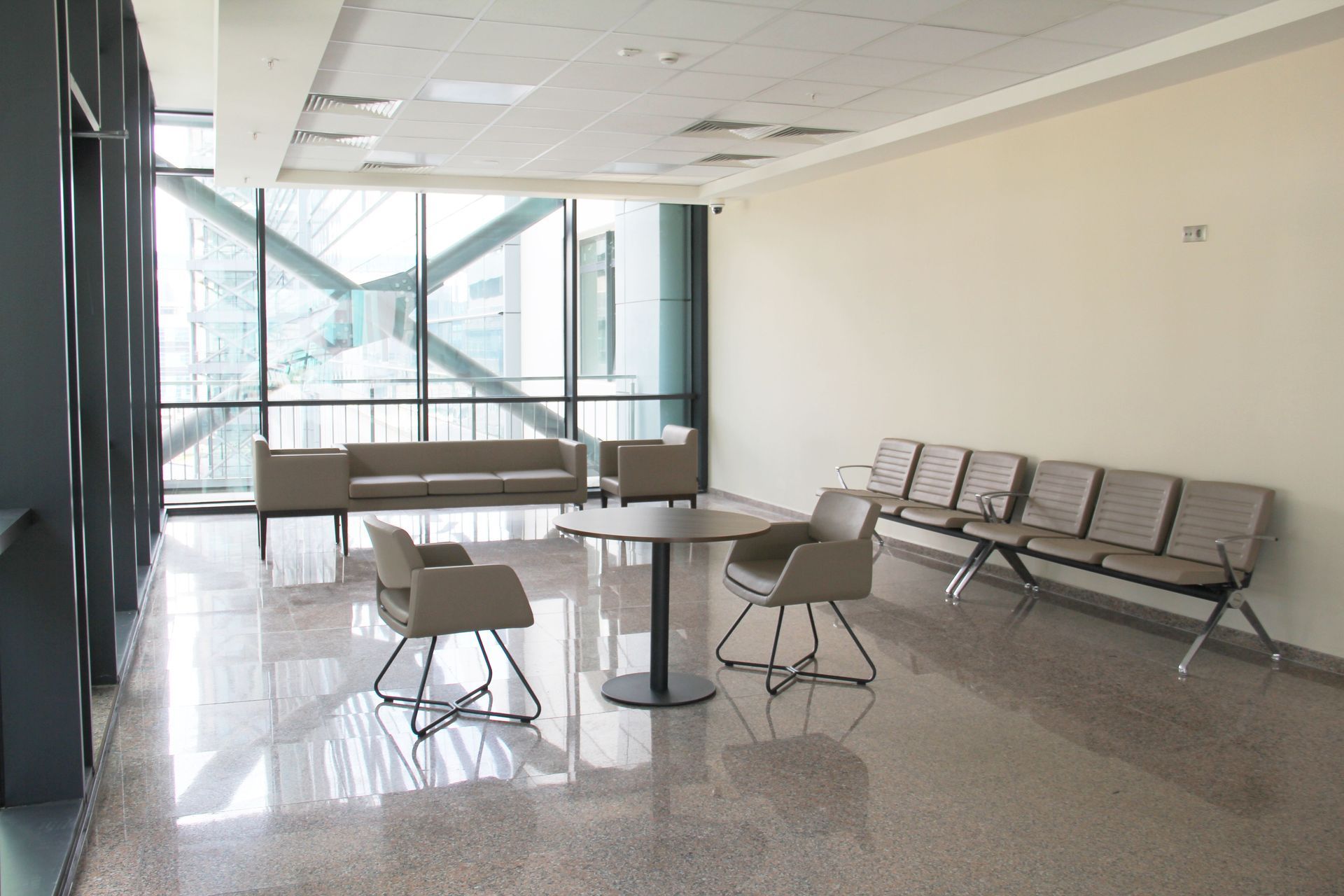 Empty airport waiting area with metal chairs, tables, and large windows overlooking stairs