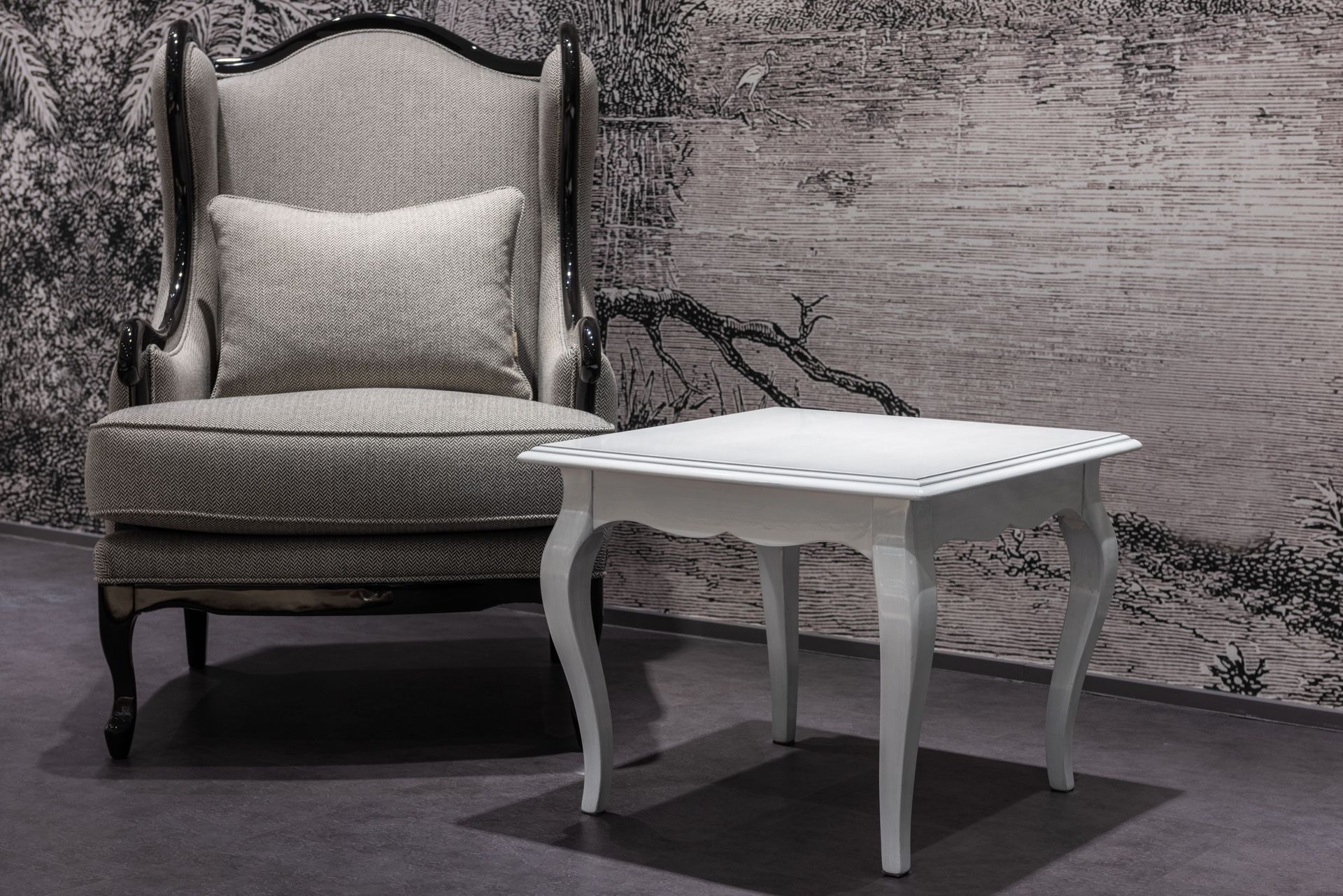 A gray upholstered armchair beside a small white side table against a textured gray wall.
