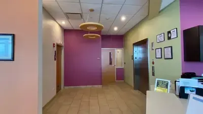 Modern office lobby with purple walls, beige tile floor, and reception desk near an elevator.