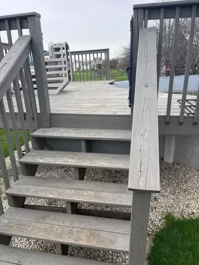 Wooden stairs leading up to a deck with gray railings and a grassy yard below.