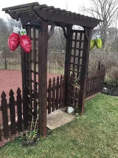 Rustic garden arbor with hanging red and green birdhouses beside a wooden picket fence and lawn