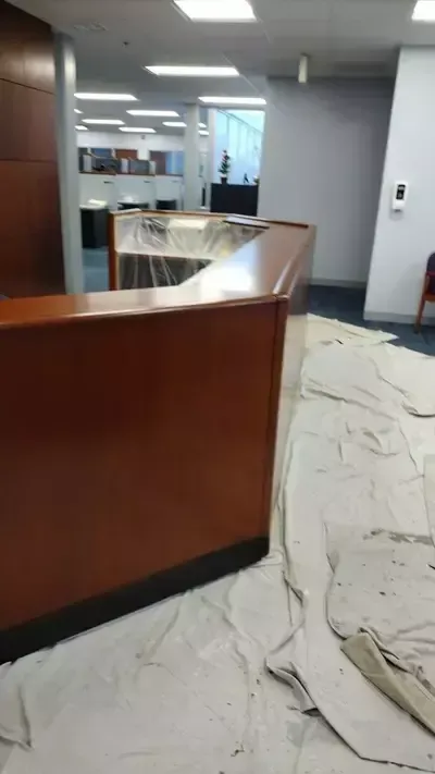 Office lobby with curved wooden reception desk, white floor covering, and hallway beyond