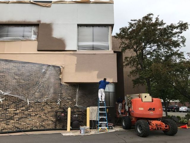 A man on a ladder is painting the side of a building