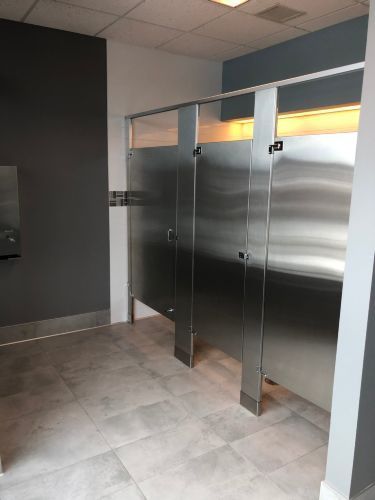 A public restroom with stainless steel stalls and a toilet paper dispenser.