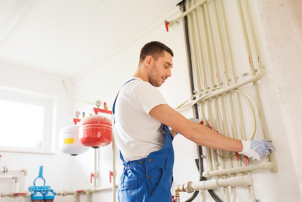 A Man Is Working On A Heating System In A Room — Gold Coast City Plumbing In Scenic Rim, QLD