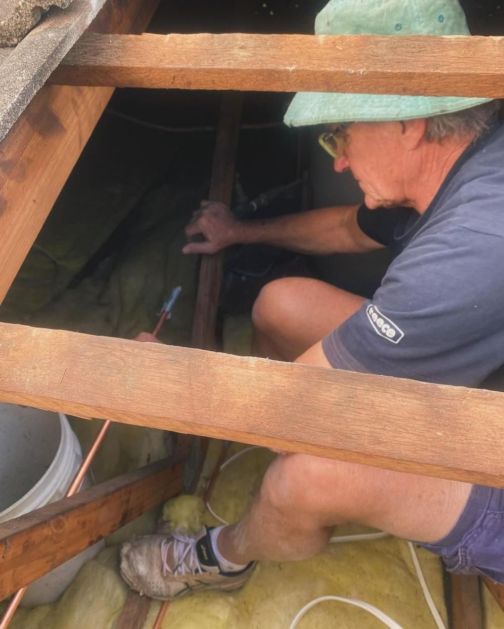 A Man Wearing A Green Hat Is Working On A Wooden Structure — Gold Coast City Plumbing In Helensvale, QLD