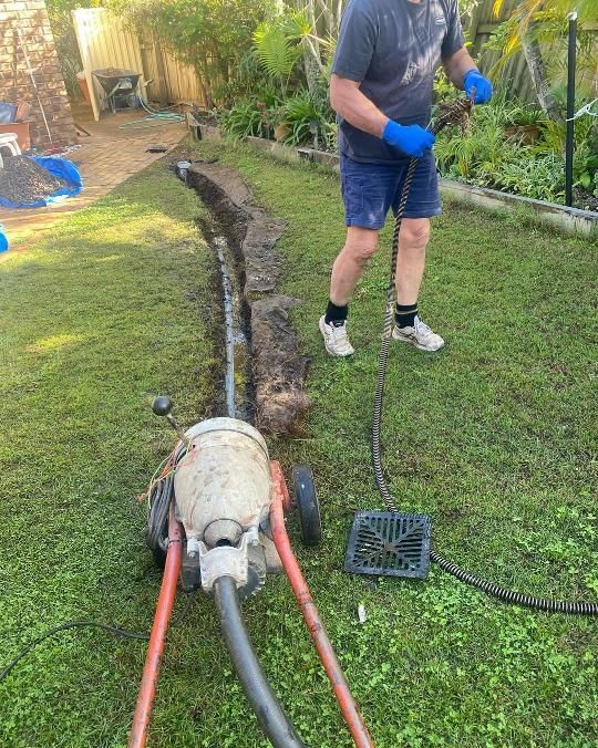 A Man Is Using A Machine To Remove A Drain In A Backyard — Gold Coast City Plumbing In Helensvale, QLD