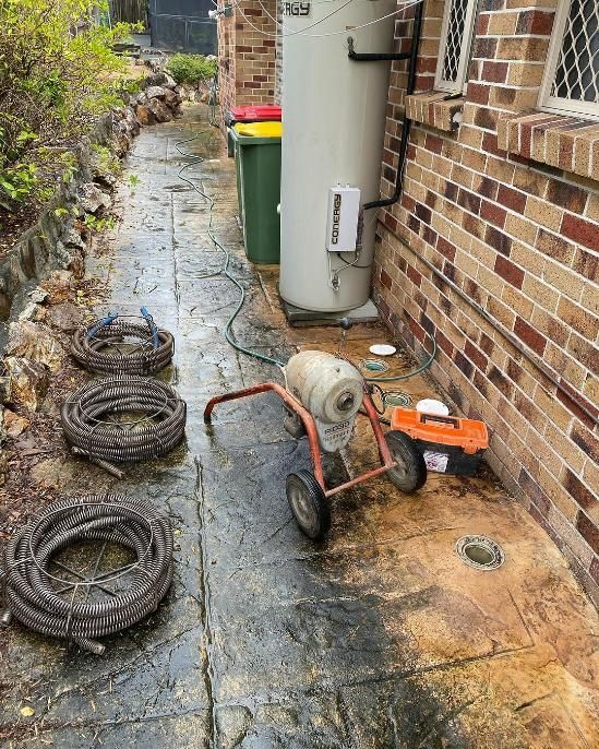 A Drain Cleaner Is Sitting On The Sidewalk Next To A Brick Wall — Gold Coast City Plumbing In Helensvale, QLD