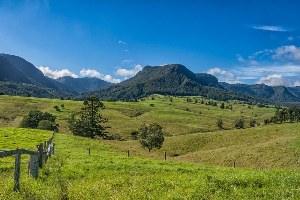 A Fence Surrounds A Grassy Field With Mountains In The Background — Gold Coast City Plumbing In Scenic Rim, QLD