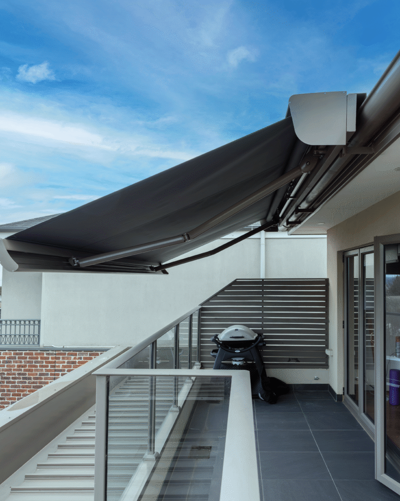 A home with brick columns and dark outdoor shades; a grassy lawn and clear blue sky.
