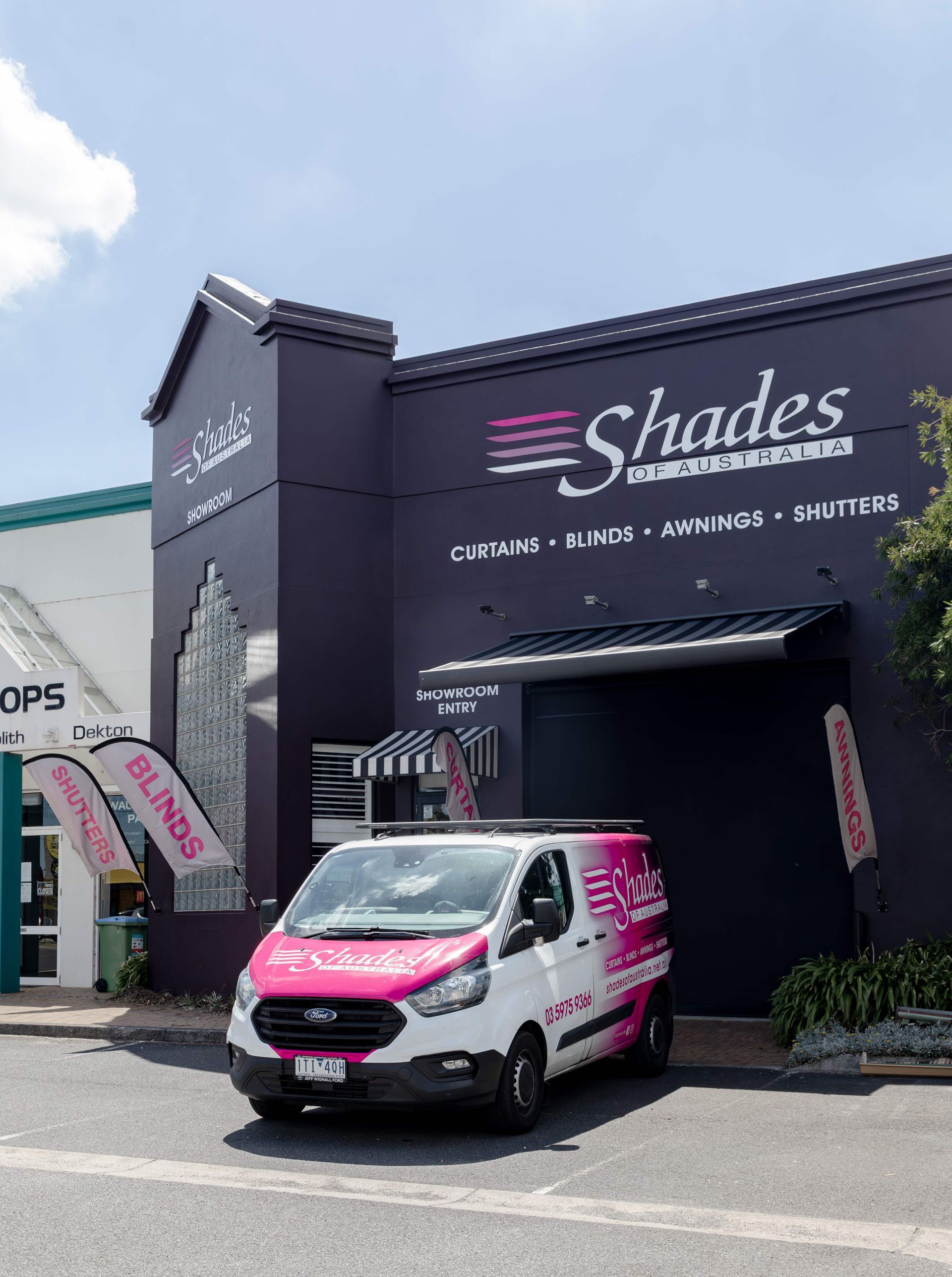 White and pink van parked in front of Shades business building; sells curtains, blinds, and awnings.