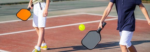 Two people are playing pickleball on a tennis court.