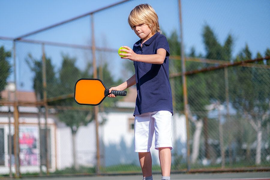 A young boy is holding a paddle and a tennis ball