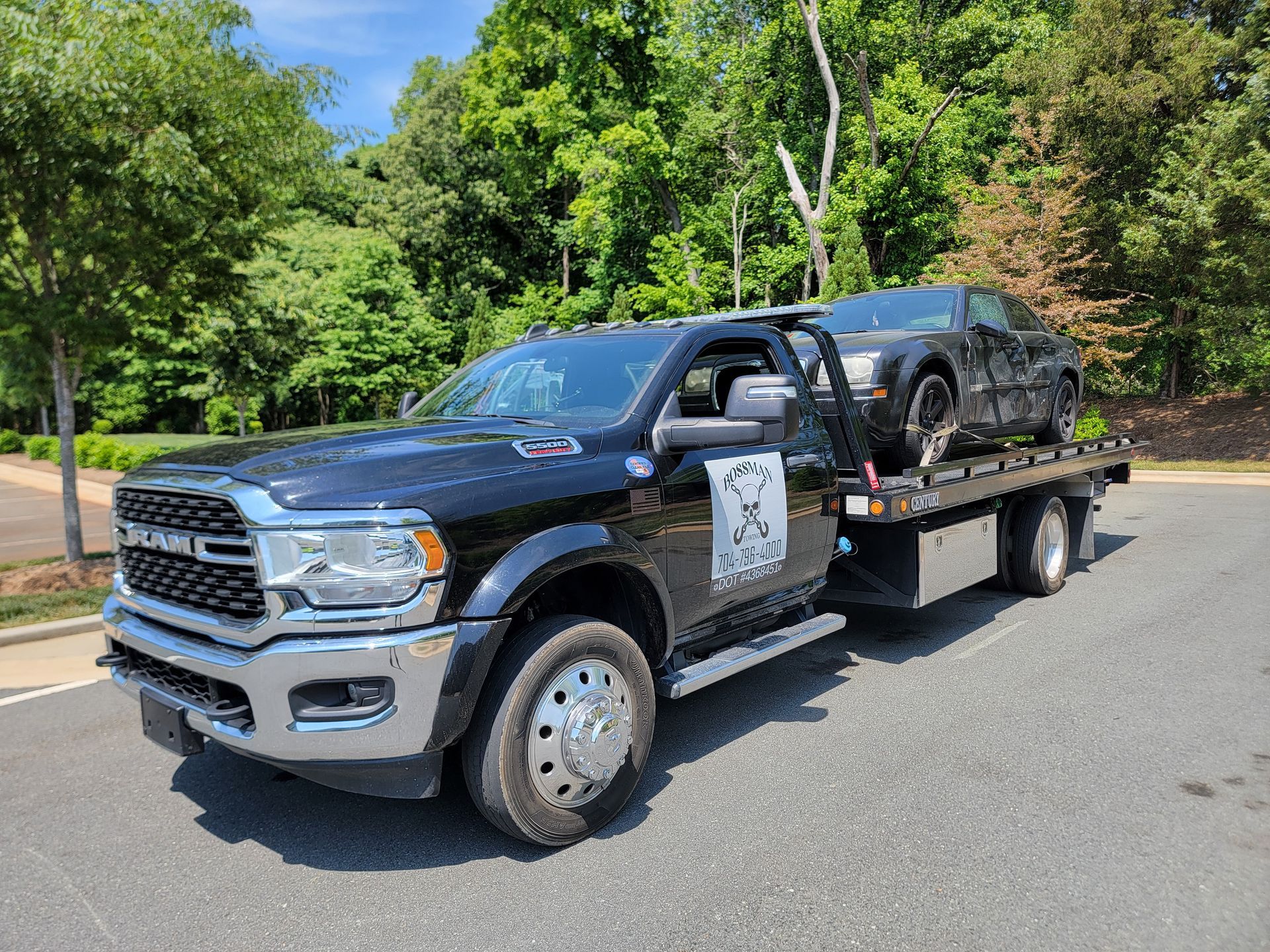 A black tow truck with a car on the back is parked on the side of the road.