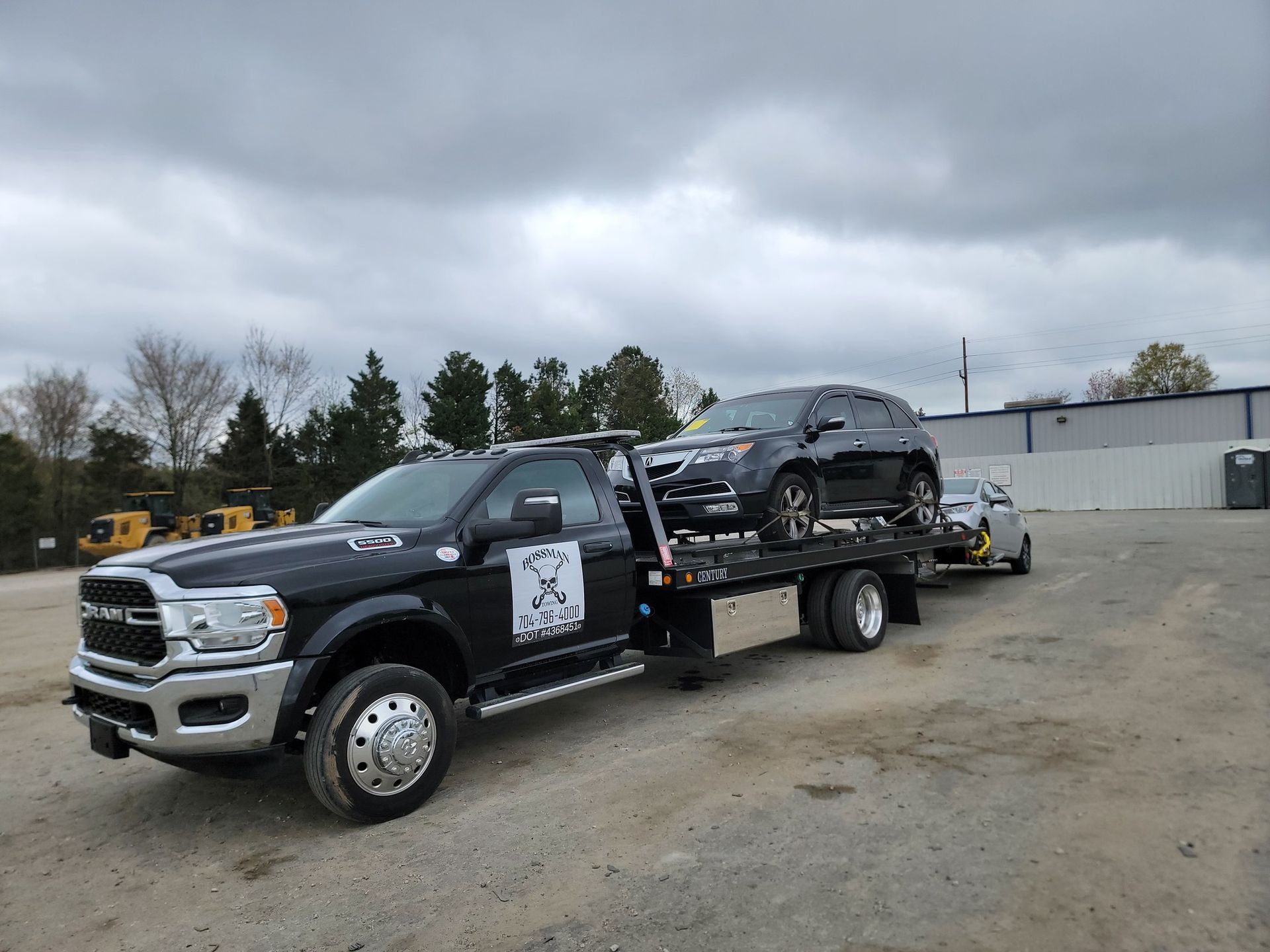 A tow truck is carrying two cars in a parking lot.