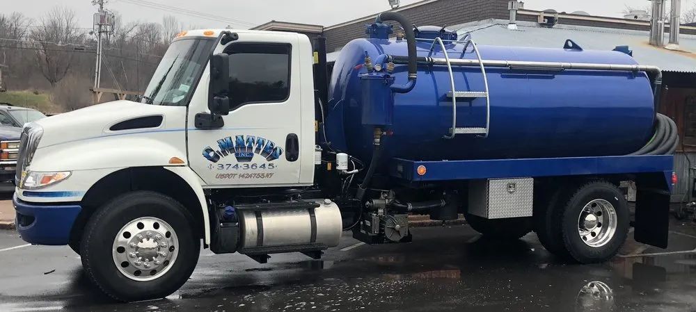 White and blue septic truck parked on wet pavement.