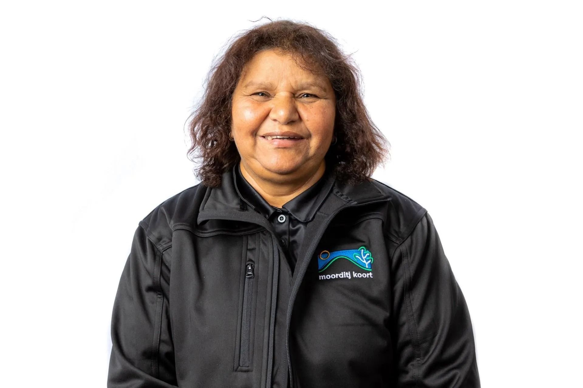 Woman with brown hair and a black jacket, smiling at the camera. White background.